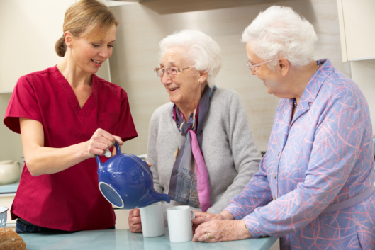 a nurse serving tea to two seniors